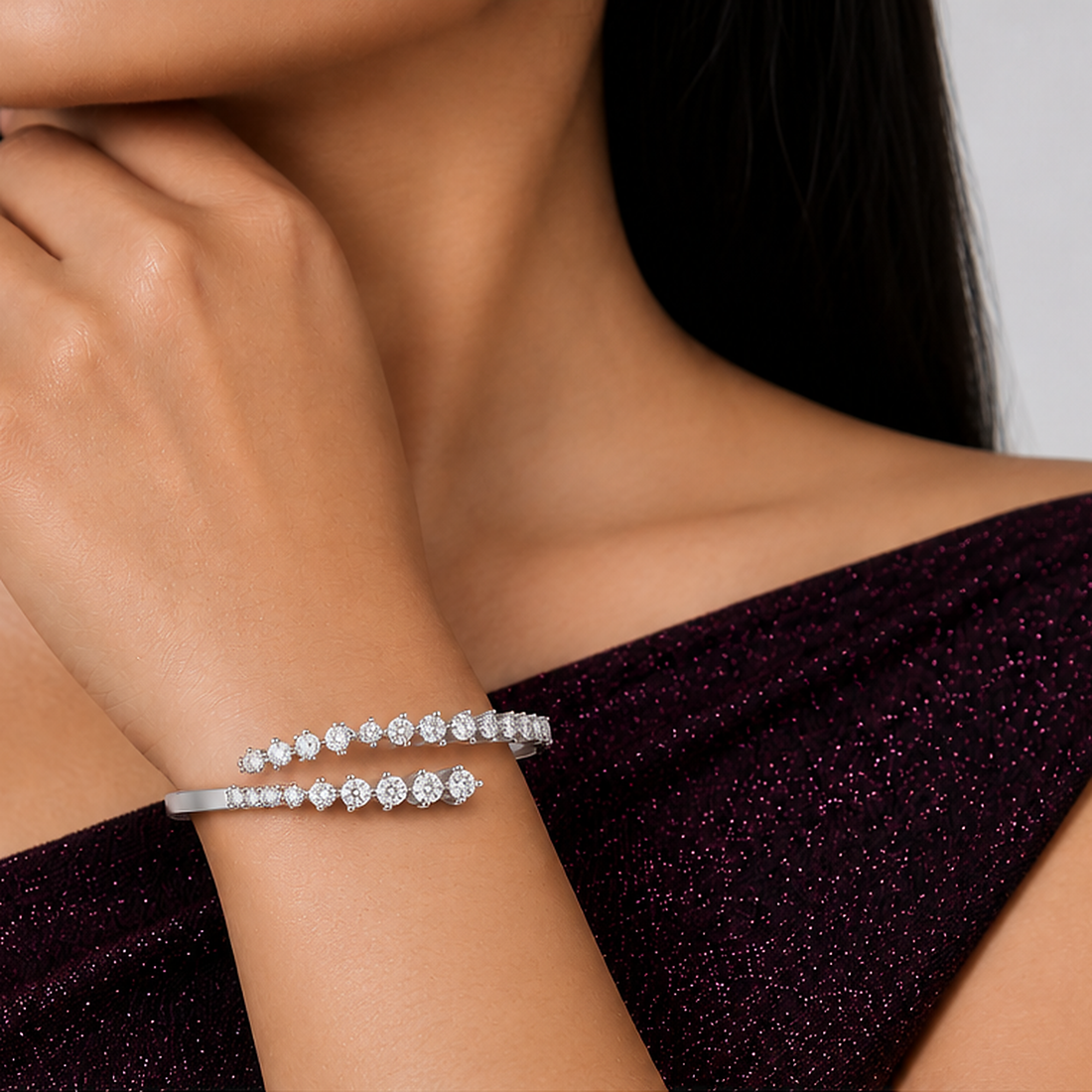 A close-up of a model's wrist wearing a slim silver cuff bracelet adorned with two rows of sparkling round-cut clear stones, paired with a dark plum off-the-shoulder top.